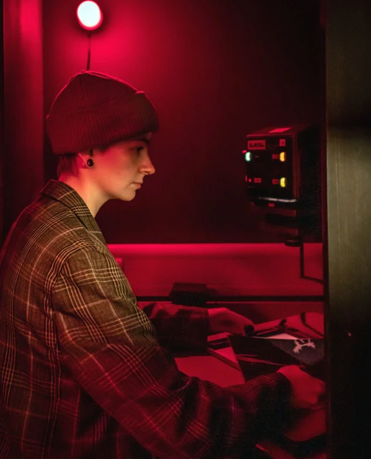 Student working with an enlarger in the darkroom, lit by a red safelight. Student working with an enlarger in the darkroom, lit by a red safelight.